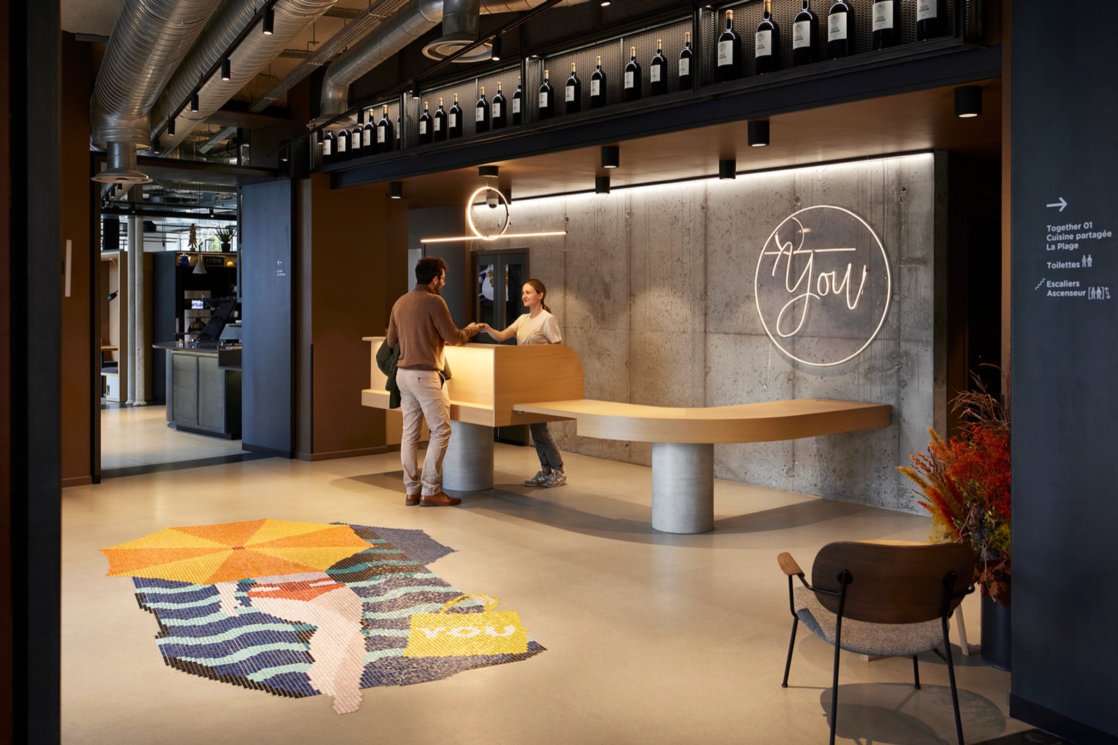 Réception d'un hôtel YOU, comptoir en bois et enseigne lumineuse